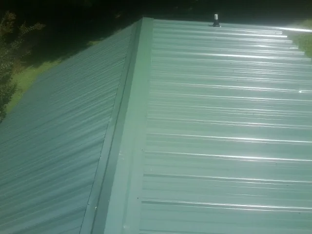 New green metal panels meeting at the ridge of a roof — Flat Roof Repair work by our crew in Groveland